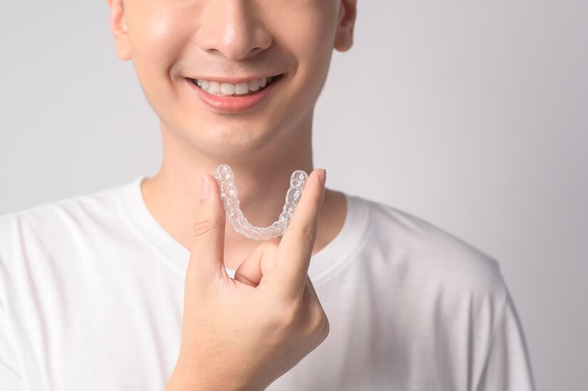 A happy person smiling after the perfect Invisalign treatment holding clear aligners